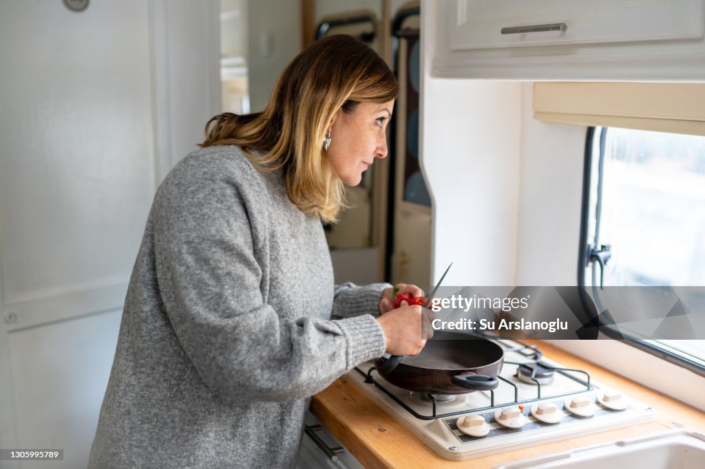 Adult woman looking out of the window and thinking about her life and future in her caravan while preparing meal