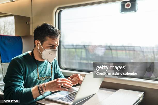 man with covid-19 protective mask working with laptop while traveling by train - mask stock-fotos und bilder
