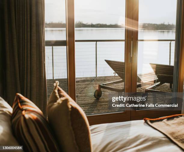 luxurious bedroom with sliding doors leading out onto decking beside a lake - sliding door stock pictures, royalty-free photos & images