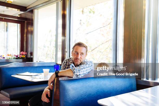 father and son sitting in booth at diner - diner foto e immagini stock