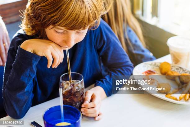 boy drinking soda through straw in restaurant - children restaurant stockfoto's en -beelden