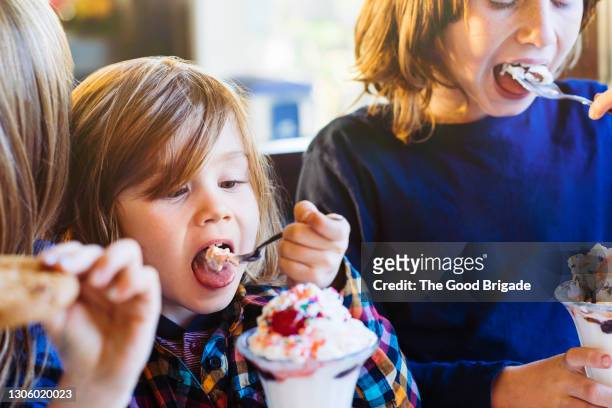 cute little boy eating ice cream with siblings in restaurant - ice cream sundae stock pictures, royalty-free photos & images