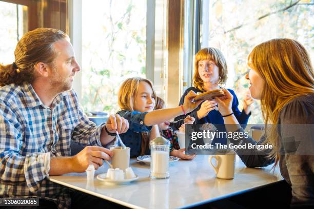 cute girl feeding cookie to mother while sitting with family in restaurant - sisters feeding stockfoto's en -beelden