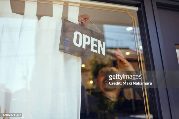 a male owner hangs an open sign on a glass door. - geschäftseröffnung stock-fotos und bilder