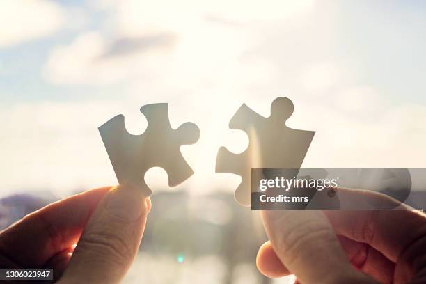 hands trying to fit two puzzle pieces together - puzzel stockfoto's en -beelden