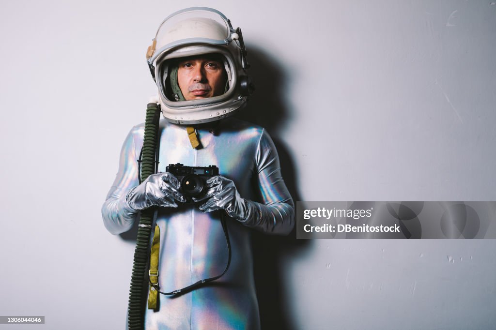 Man wearing silver tight suit and retro astronaut helmet, holding old photo camera