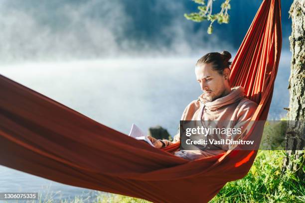 mann in hängematte lesen ein buch. entspannung im naturkonzept. - kleiner hügel stock-fotos und bilder