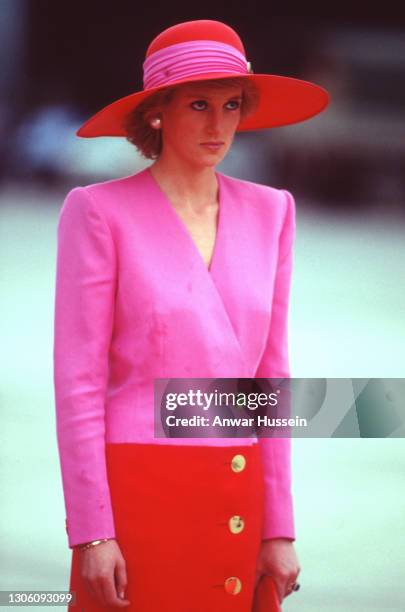 Diana, Princess of Wales, wearing a pink and red coat dress with gold buttons designed by Catherine Walker and a matching hat designed by Philip...