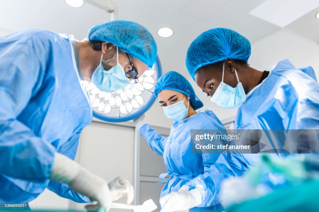 Preparation for the beginning of surgical operation with a cut. Group of surgeons at work in operating theater toned in blue. Medical team performing operation