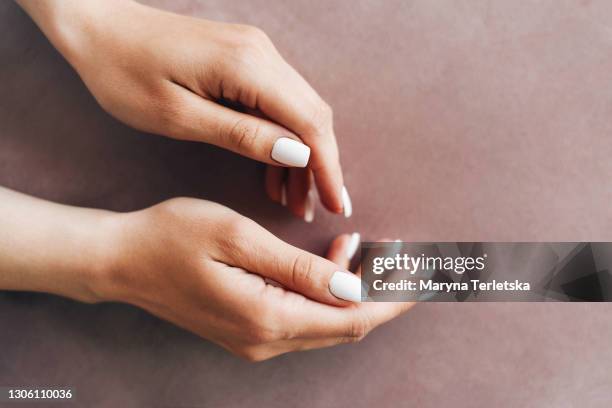 female hands with a neat white manicure on a beige background. - gel foto e immagini stock