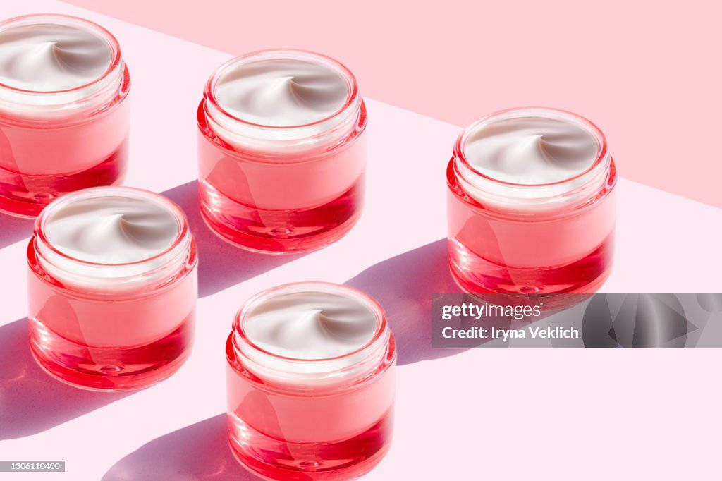 Trendy Pattern made of Beauty product cream in pink color bottle on pastel pink background.