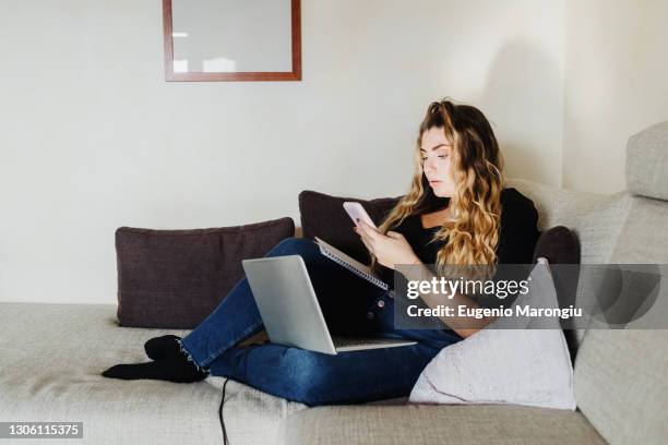 young woman using smartphone and laptop at home - hourglass books fotografías e imágenes de stock