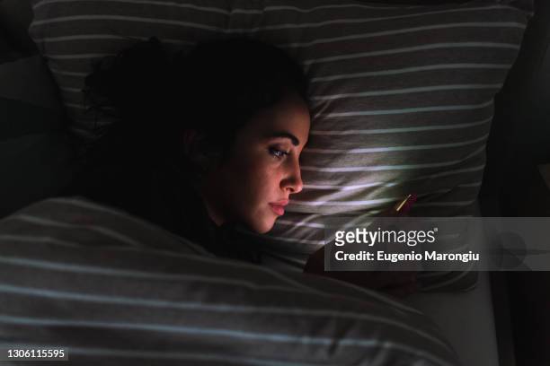 young woman lying in bed and looking at phone - quarantine stock pictures, royalty-free photos & images