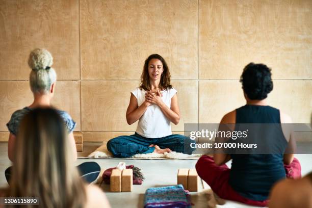 yoga instructor with hands clasped teaching class - meditieren stock-fotos und bilder