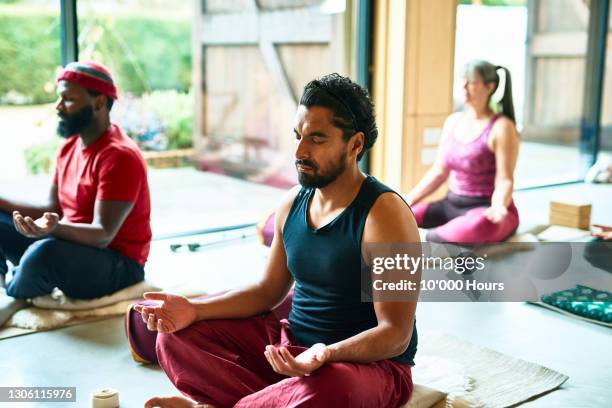 mid adult man meditating in yoga class - meditieren stock-fotos und bilder