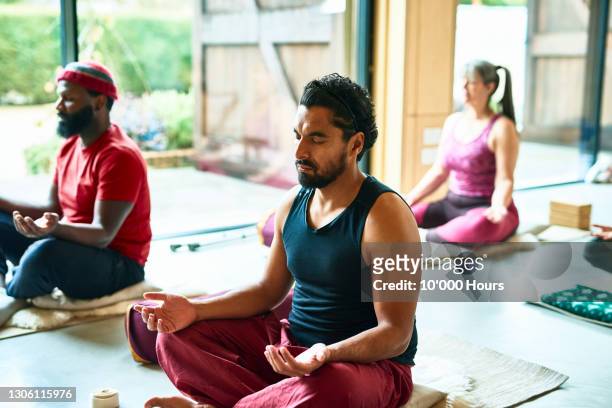 mid adult man meditating in yoga class - meditation stock pictures, royalty-free photos & images