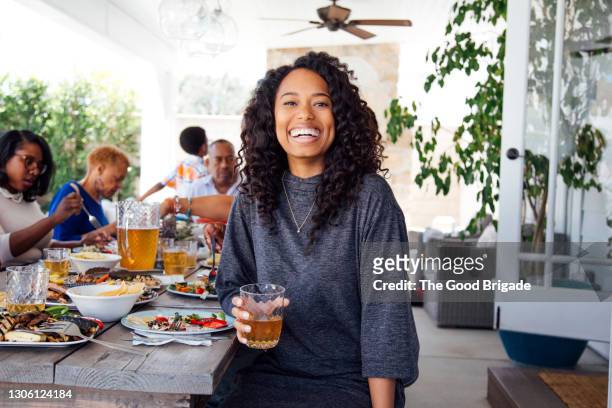 portrait of smiling woman with drink at outdoor family party - sitting at table looking at camera stock-fotos und bilder