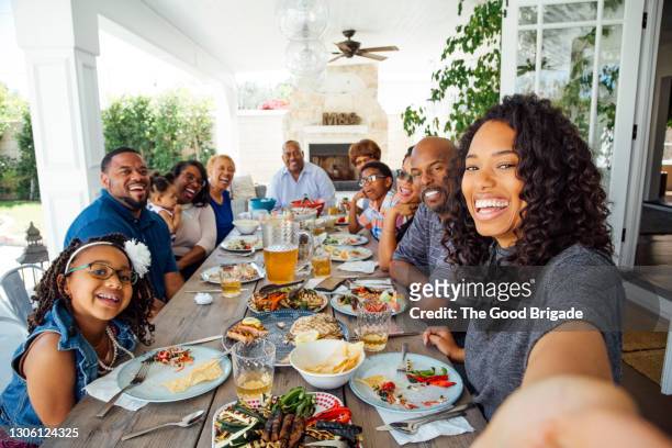 smiling woman taking selfie with family at dinner party - black family reunion stock pictures, royalty-free photos & images