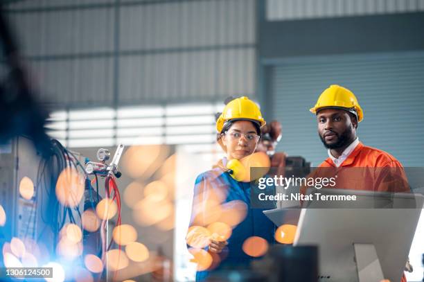 male african engineers and female asian trainee engineer having a meeting in front of industrial robots welder in production line. - work accountability stock-fotos und bilder