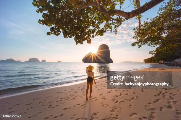 a young woman standing and looking on the rock in railay east beach in the golden twilight time moment, krabi province, thailand - beach holiday stock-fotos und bilder