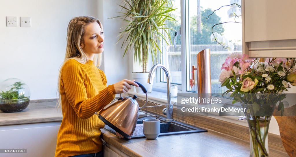 La jeune femme blonde attirante romantique rêveuse se tient à la fenêtre de cuisine et regarde dans la distance
