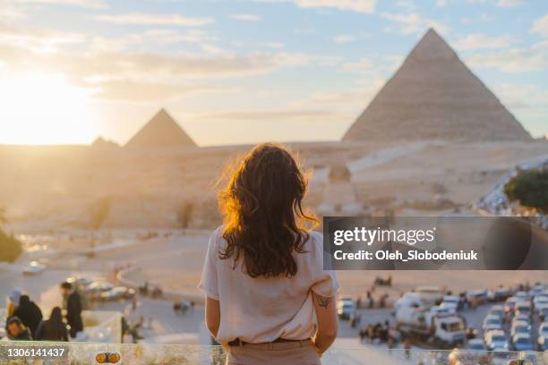 vrouw die zich op het terras op de achtergrond van de piramides van gizeh bevindt - pyramid shape stockfoto's en -beelden