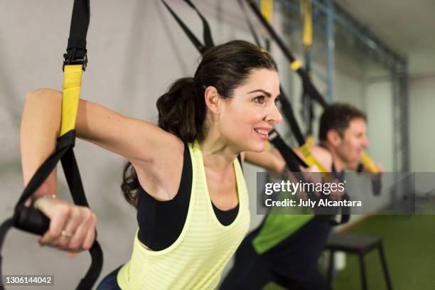 aantrekkelijke 40-jarige vrouw en man voert schorsingstraining uit in sportschool - suspension training stockfoto's en -beelden