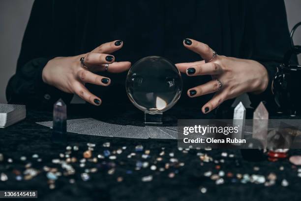 the hands of a young woman conjure over a transparent sphere surrounded by tarot cards - witch stock pictures, royalty-free photos & images