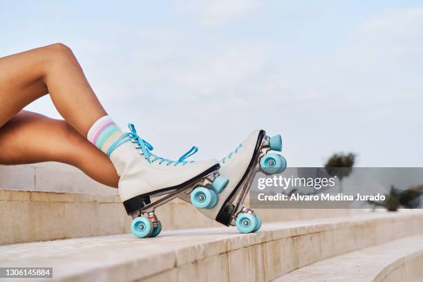 woman in stylish retro roller skates sitting on the steps on urban seafront - rolschaatsen schaats stockfoto's en -beelden
