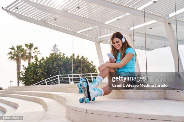 happy young woman in quad roller skates resting on stairs while using your smartphone - one embankment stock-fotos und bilder