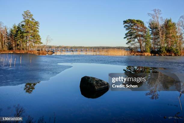 a footbridge in a lake during ice melt and a rock in the foreground in the sun in spring - vaxjo stock-fotos und bilder
