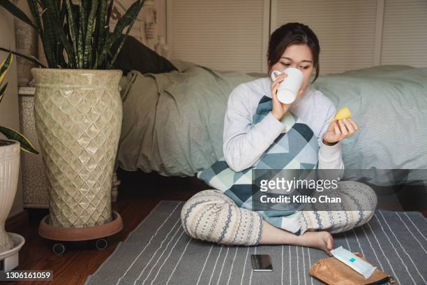 asian woman holding a menstrual cup while drinking water in her bedroom - menstrual cup stock pictures, royalty-free photos & images