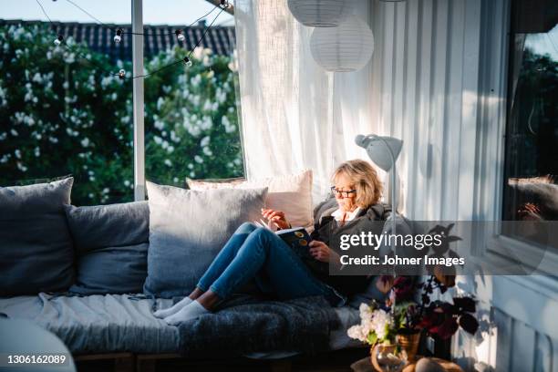 woman sitting on sofa in conservatory - reading stockfoto's en -beelden