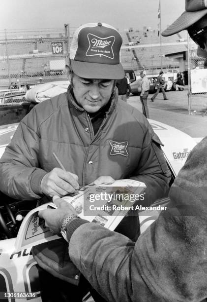 Driver Bobby Allison signs an autograph in the speedway garage area prior to the start of the 1983 Daytona 500 stock car race at Daytona...
