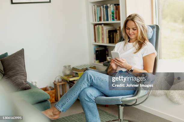 smiling woman using cell phone on chair - donne bionde scalze foto e immagini stock