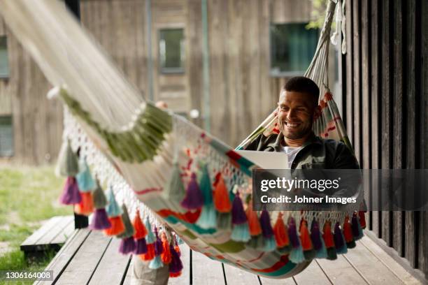 smiling man using laptop while relaxing on hammock - surfing the net fotografías e imágenes de stock