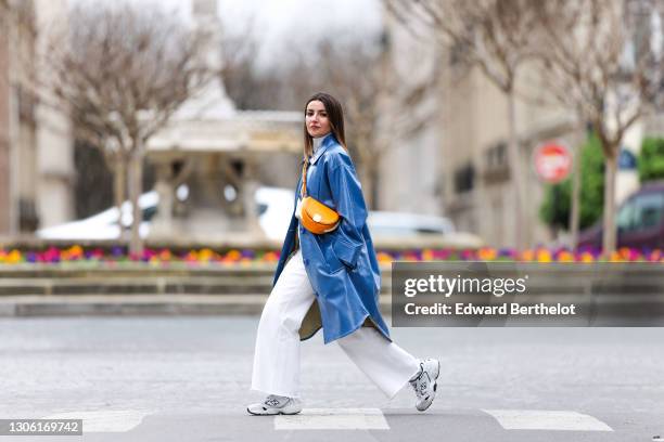 Alexandra Pereira wears a white turtleneck pullover / sweater from Zara, a blue long trench coat from Stand Studio, white flare denim jeans from...