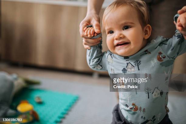 nette kleine lächelnde baby junge glücklich für seine ersten schritte - hand in hand spazieren stock-fotos und bilder