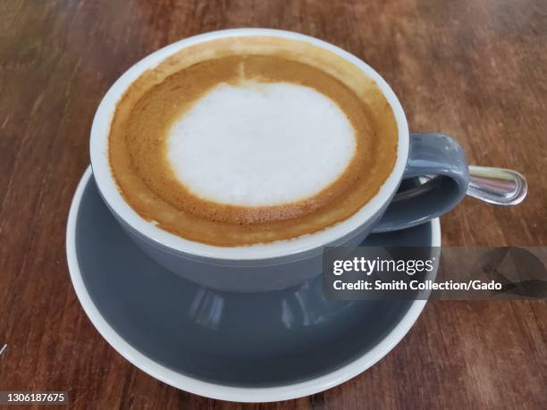 Close-up shot of an oat milk latte served in a cup on a saucer with a spoon next to it in Lafayette, California, February 23, 2021.