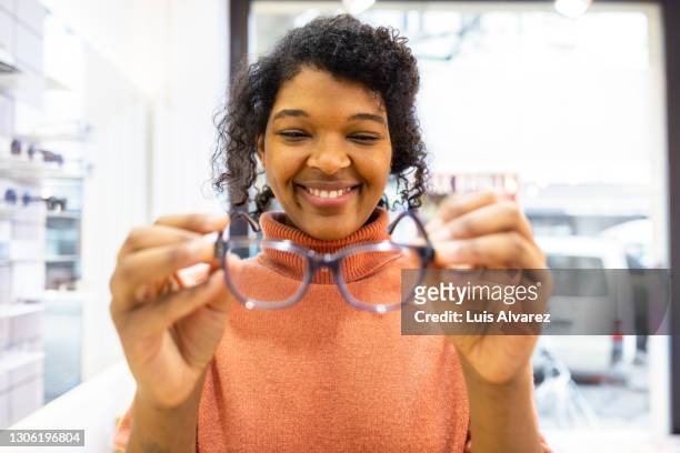 female customer choosing new pair of glasses in optician shop - spectacles stock pictures, royalty-free photos & images