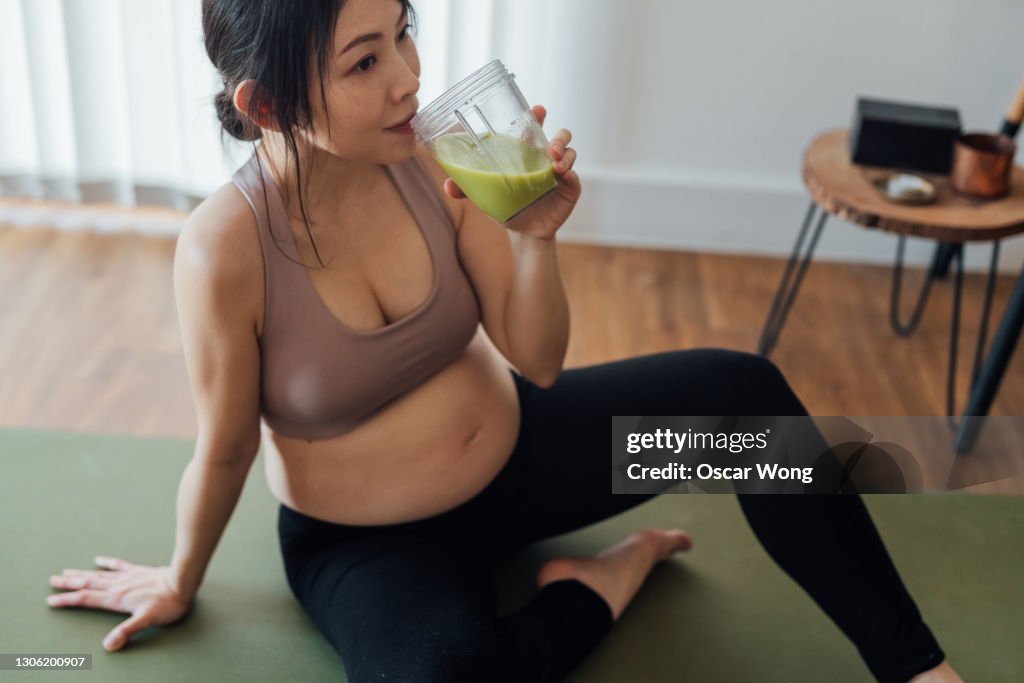 Young woman taking rest and having fresh home-made green smoothie after a yoga session at home