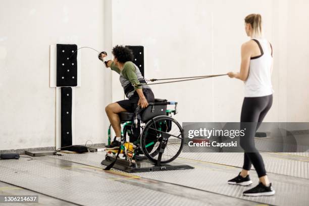 Entrenadora femenina ayudando a atleta masculino de esgrima en silla de ruedas en el entrenamiento