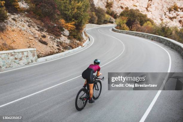 rear view of woman cycling on mountain highway on road triathlon bicycle - extreme sports bike stock pictures, royalty-free photos & images