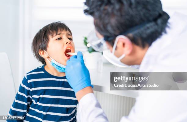 male pediatrician examining little child patient’s throat at clinic - sticking out tongue stock pictures, royalty-free photos & images