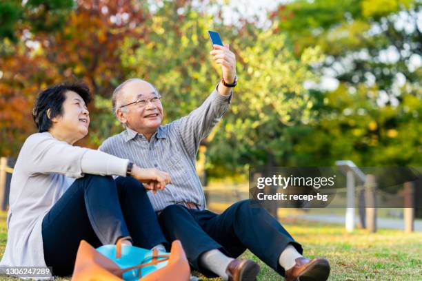 シニア大人は、公共の公園でリラックスしてスマートフォンを使用してカップルを楽しんで - 夫婦 ストックフォトと画像