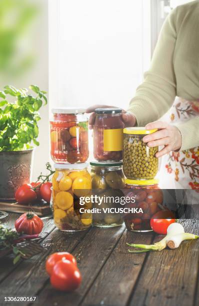 women holding many preserve jars with canned vegetables on wooden kitchen table with ingredients at window background. - preserving stock pictures, royalty-free photos & images