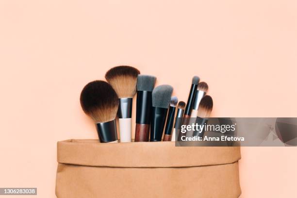 top view of set of assorted soft brushes for makeup application placed in paper bag on peach coral beige background. flat lay style. cosmetic banner with copy space. wooden handles and natural bristle are the best choice for zero waste concept. cruelty-fr - vanity bag stock pictures, royalty-free photos & images