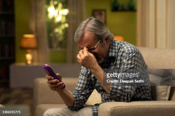 shot of mature man sitting on sofa watching tv- stock photo - indian football stock pictures, royalty-free photos & images