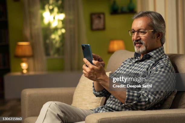 shot of a mature man using mobile phone sitting on sofa at home:- stock photo - senior adult on phone stock pictures, royalty-free photos & images