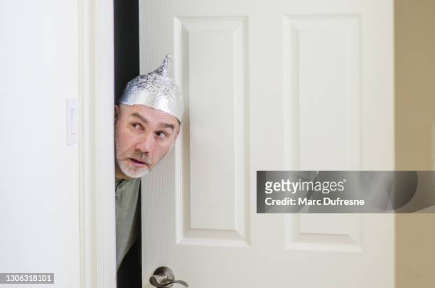 man with aluminum foil hat behind door - hat stock pictures, royalty-free photos & images